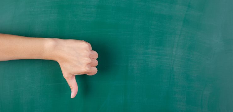 Closeup of woman's hand gesturing thumbs down against chalkboard